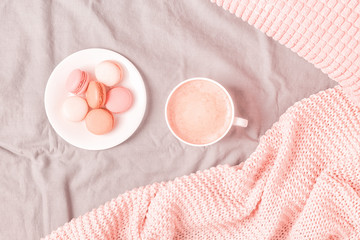 Bed with pink knitted plaid, coffee and macaroons.