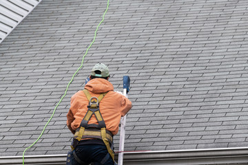 House during day with gray color Single Family Home and man walking on roof shingles and ladder...