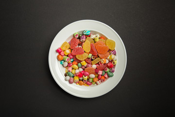 top view of delicious multicolored caramel candies and citrus jellies in white plate on black background