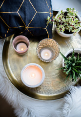 Cozy real home decoration, burning candles on golden tray with pillow on white faux fur on windowsill