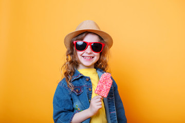Portrait of beautiful happy little girl in red sunglasses with ice cream on orange background