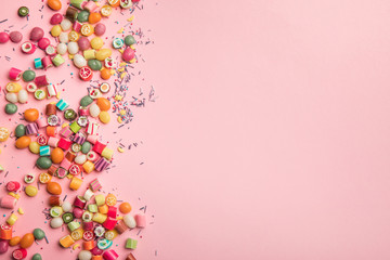 top view of multicolored candies and sprinkles scattered on pink background with copy space