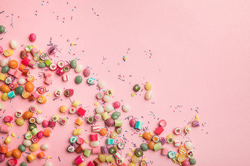 Obraz na płótnie Canvas top view of colorful candies and sprinkles scattered on pink background with copy space