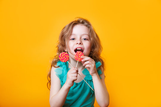 Funny child with candy lollipop, happy little girl eating big sugar lollipop on yellow bright background,