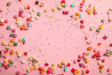top view of multicolored candies and sprinkles scattered on pink background