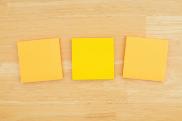 Three blank sticky notes on textured desk wood background