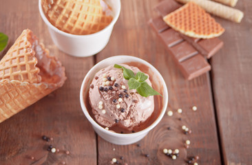 Paper bowl of chocolate ice cream, waffle cones and spoon for ice cream on wooden background. Top view.