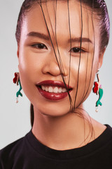 Shot of smiling Asian lady, wearing black T-shirt and massive earrings in view of a storybook...