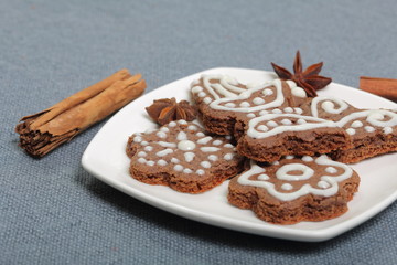 Gingerbread cookies decorated with a pattern of white glaze. On a background of gray fabric. Decorated with decorative elements of cinnamon sticks and anise stars.