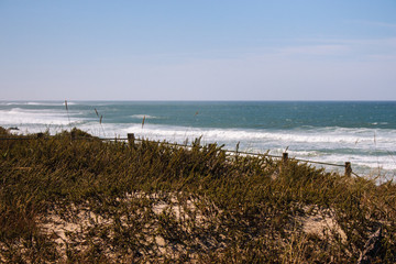 Panoramic landscape of Atlantic Ocean coast. Wide beach with waves and grass coast with fence. Summer coastline. Seascape concept. Travel and vacation concept. Portugal nature. 