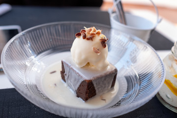 piece of dark chocolate with a ball of vanilla ice cream decorated with nuts on white chocolate background