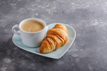 Cup of coffee and freshly baked croissants on gray background. Copy space.