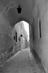 Tunnel with a lantern in a narrow street in the old historical town of Mdina in Malta. Black and white