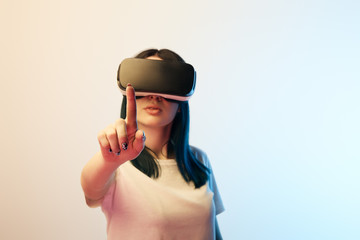 selective focus of girl pointing with finger while wearing virtual reality headset on beige and blue