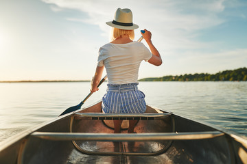 Young woman canoeing on a sunny afternoon in summer - obrazy, fototapety, plakaty