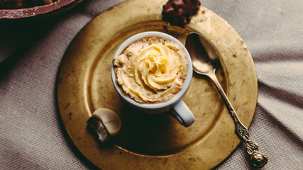 A cup of coffee with vanilla cream on a golden plate with a spoon. Chocolates, chocolate