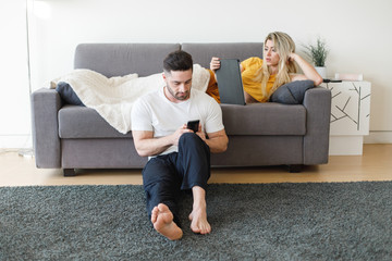 Young casual couple using mobiles phone and tablet at home
