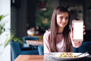 Young woman showing white phone screen in a restaurant