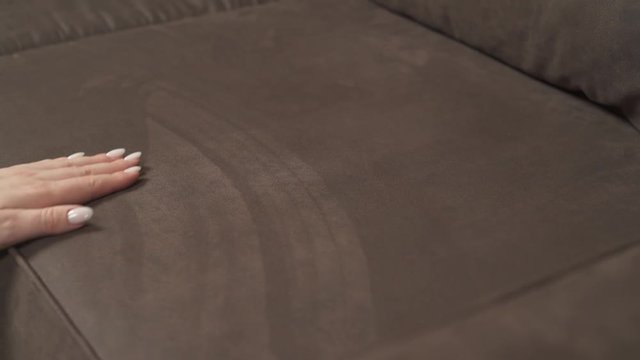 Female hand with manicure touches couch upholstery. A gentle touch of a hand on a brown pillow. Isolated, close-up demonstration