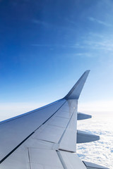 Fototapeta na wymiar Window view of aircraft wing flying over clouds in blue sky