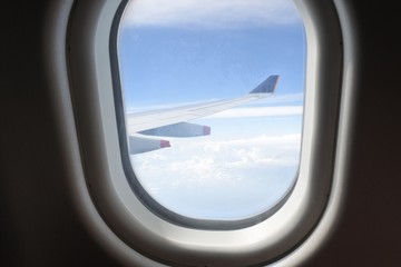 Fototapeta na wymiar window of the airplane,a view of wing of commercial airplane flying above white cloud and blue sky