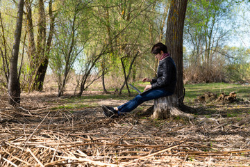Naklejka na ściany i meble Girl using lap top among nature. Time online. Is sits on a stump near a tree