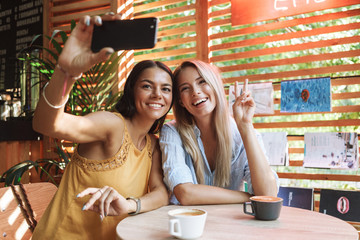 Two cheerful young girlfriends sitting at the cafe indoors