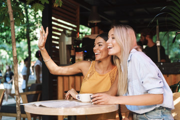 Two cheerful young girlfriends sitting at the cafe table