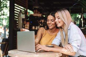 Two cheerful young girlfriends sitting at the cafe indoors