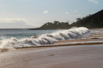 Brandung am Strand mit Sonne und Berge im Hintergrund