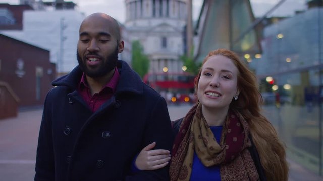 Young diverse couple walk arm in arm in the city one evening, in slow motion