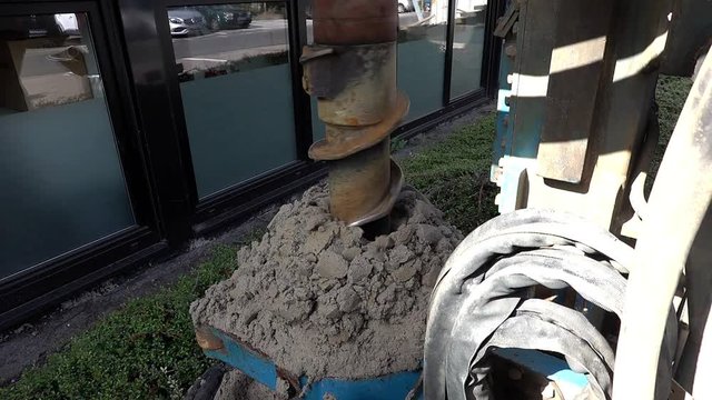 Hollow borehole auger of a dry drilling rig drills a hole in the sandy soil and produces sand on the sides.