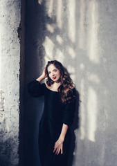 Beautiful sensual woman in dress stands by the grunge wall. 