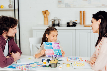 Fototapeta premium cheerful kid holding paper with colorful stripes near parents at home