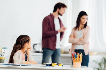 selective focus of kid looking at father quarreling with mother at home