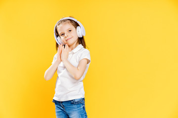 Girl of 7 years old listening to music in white wireless headphones on yellow studio background . Dancing girl. Happy small girl dancing to music. Cute child enjoying happy dance music.