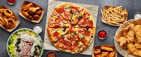 Foto op Plexiglas Eten grote tafel met diverse afhaalmaaltijden zoals pizza, frites, uienringen, gebakken kip en kippenvleugels