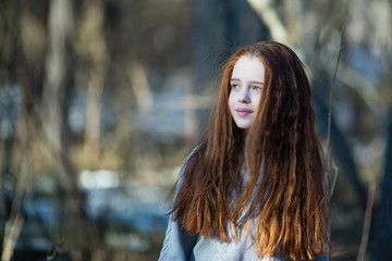 Cute teen girl with fiery red hair posing in the pine park for a photoshooting.