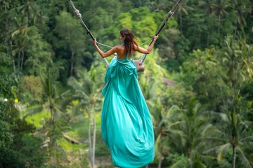 Poster Tanned young woman riding on a long swing. Island of Bali. Tropical forest on the background. Travel and joy. Close up © _KUBE_