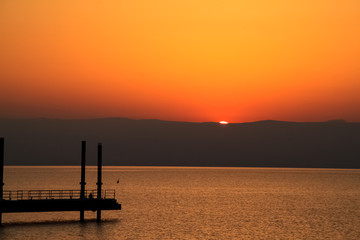 Obraz premium Tourist sits on pier watching the sunrise at Sea of Galilee