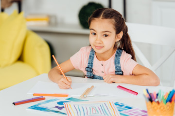 selective focus of happy child looking at camera while holding color pencil near paper at home