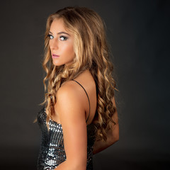 Naklejka premium Sultry, beautiful woman with long blonde hair in metallic party dress looking back over her shoulder.