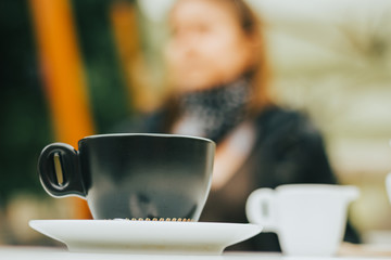 Small green coffee cup on a white plate and milk with a person in background – Stylish ceramic mug for serving hot beverages – Tasty and sweet drink in the morning