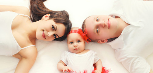 Obraz na płótnie Canvas Portrait close-up happy family mother, father with baby lying on bed or carpet at home, top view