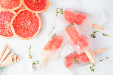 Healthy grapefruit and thyme ice pops, top view table scene scattered on a white marble background