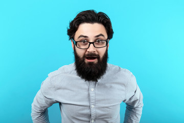 Fototapeta premium Wow! Surprised man with opened mouth, shocked guy with glasses, over blue background