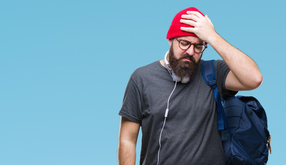 Young hipster man wearing red wool cap and backpack over isolated background suffering from headache desperate and stressed because pain and migraine. Hands on head.
