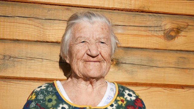 Granny chats and smiles.  Wrinkled face of aged woman. Grandmother on wooden rustic background. Old granny looks into the camera and chats. 91 year old grandmother.