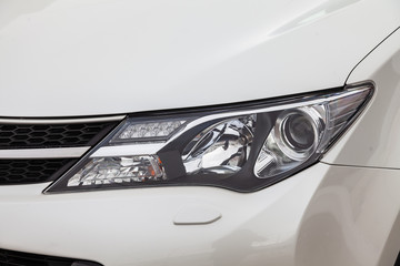 Front headlamp view of white used car stands in the auto showroom sale after washing and polish with orange turn light and led lens. Auto service industry.