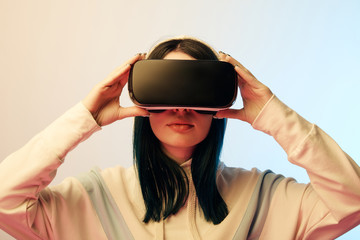 beautiful brunette young woman touching virtual reality headset on beige and blue